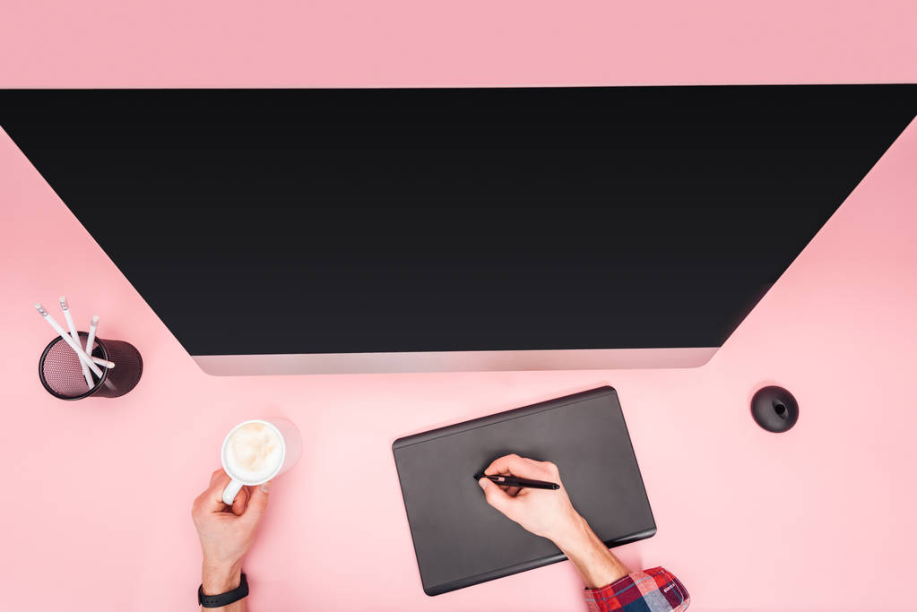 gedeeltelijke weergave van man met behulp van grafische tablet en bedrijf cup met koffie op roze achtergrond - Foto, afbeelding