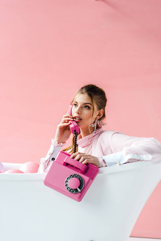 chica bonita hablando en el teléfono retro mientras se encuentra en la bañera en rosa
 - Foto, Imagen