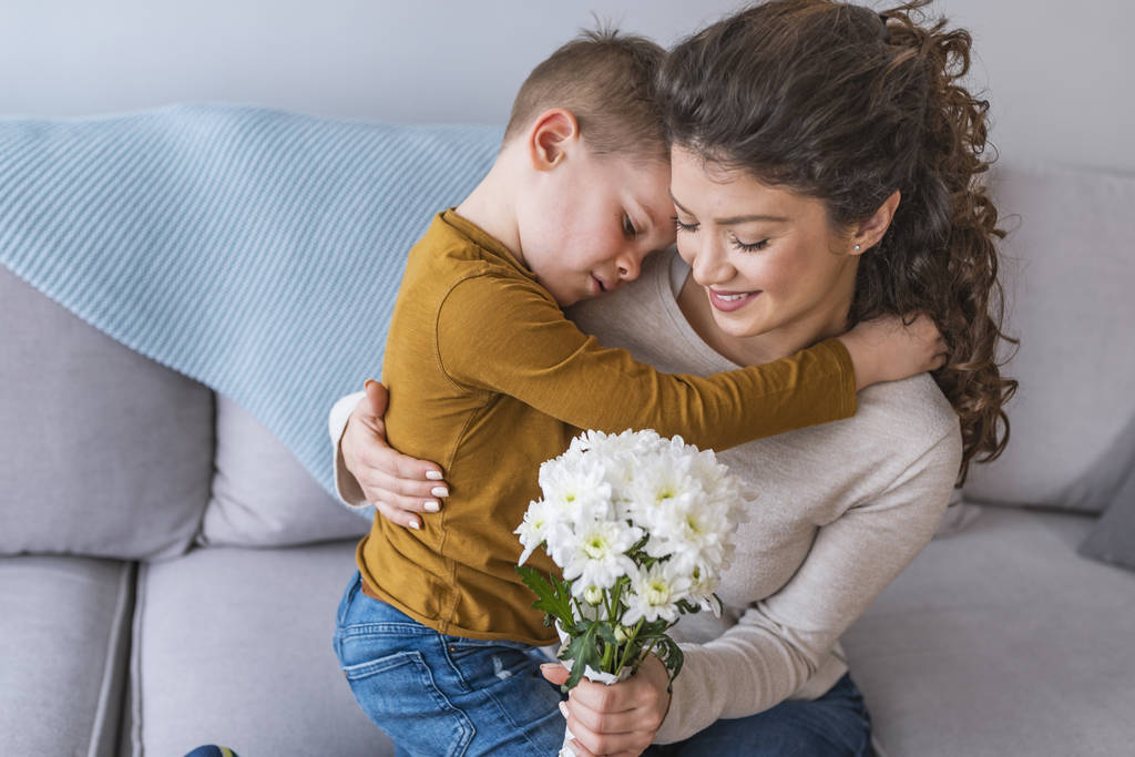 Äiti ja pieni poika kukkakimpun kanssa halaa sohvalla
 - Valokuva, kuva
