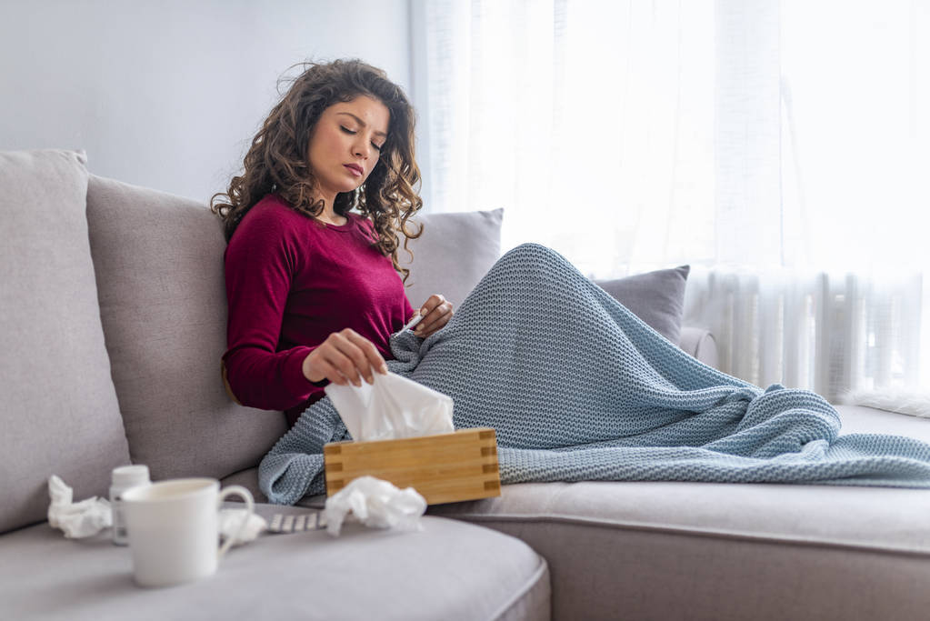 Спритна жінка сидить на ліжку, загорнута в ковдру, відчуває себе хворим на грип, має гарячку і дме нежить з носовичкою
 - Фото, зображення