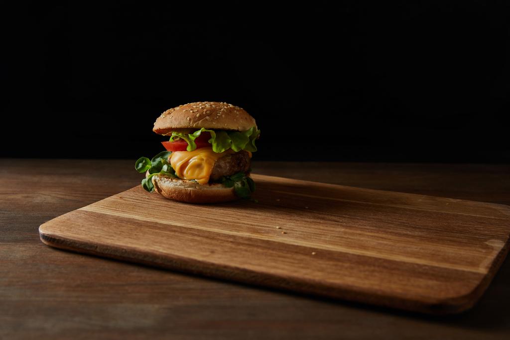 sabrosa hamburguesa de carne con sésamo sobre tabla de cortar de madera aislado en negro
 - Foto, Imagen