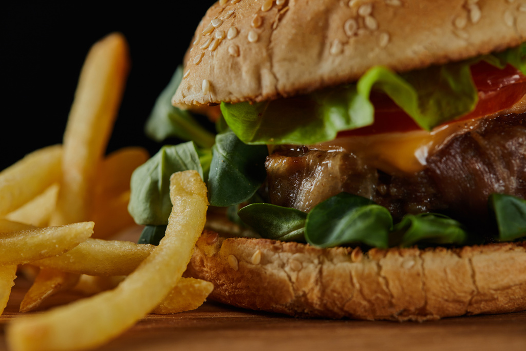 close up of delicious meat burger with cheese, greenery and sesame near french fries  - Photo, Image