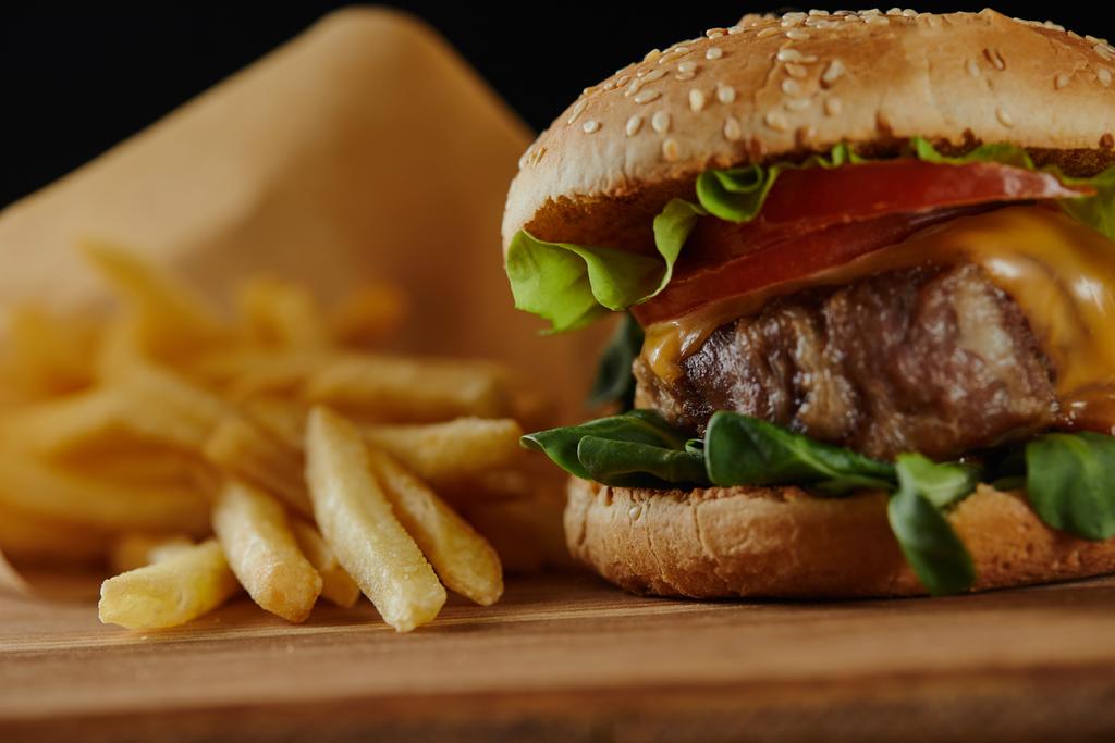 ahşap yüzeyde et ve patates kızartması ile lezzetli burger seçici odak - Fotoğraf, Görsel