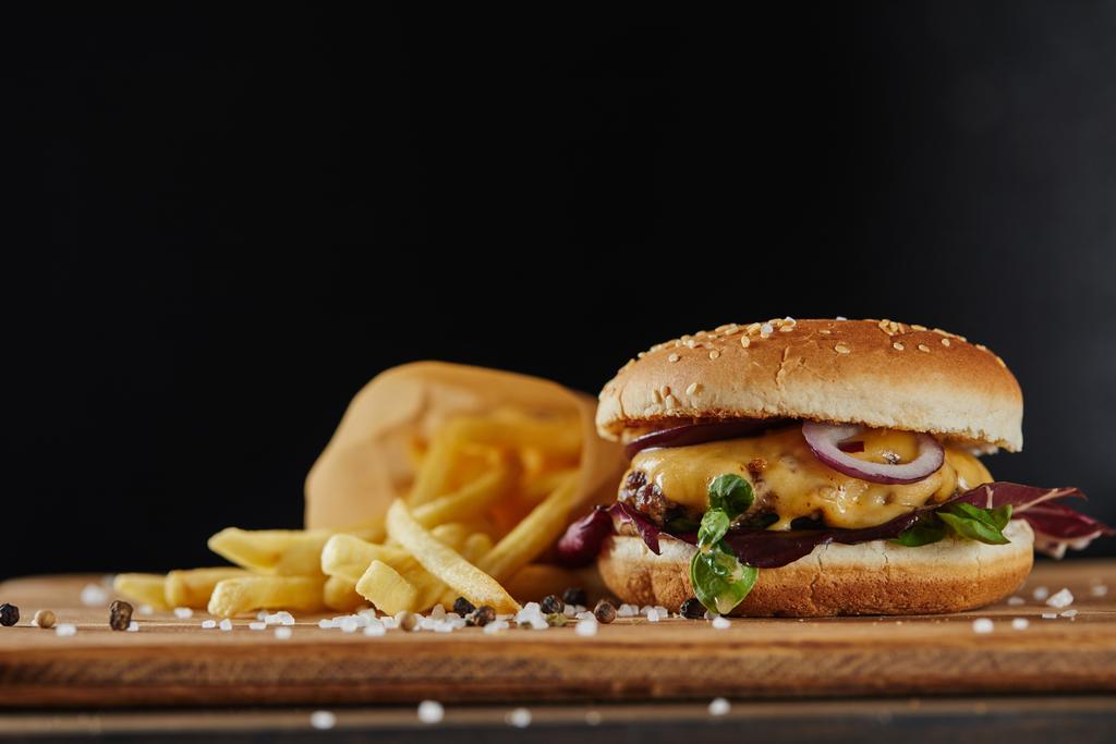 salt, french fries and delicious burger with meat on wooden surface isolated on black - Photo, Image