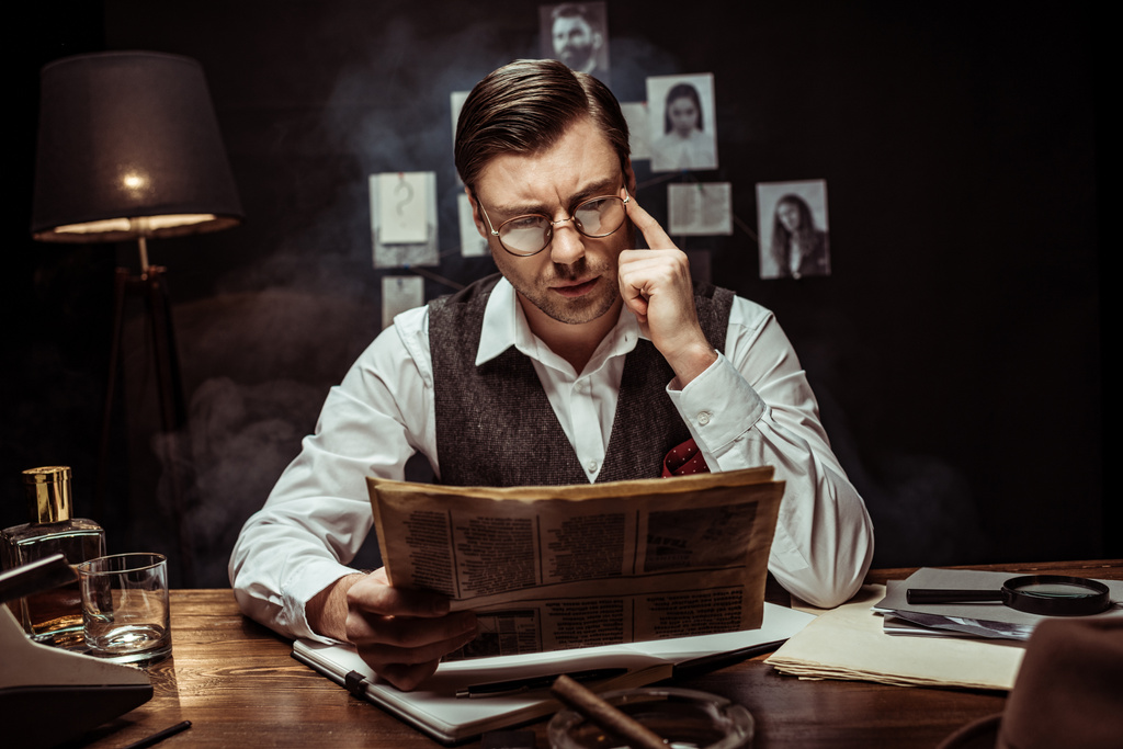 Konzentrierter Detektiv mit Brille liest Zeitung im dunklen Büro - Foto, Bild