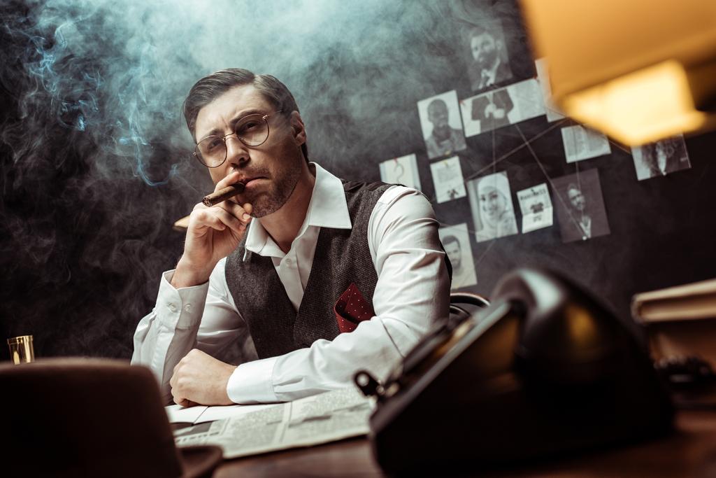 Vue à angle bas de détective coûteux dans les lunettes fumant cigare dans le bureau
 - Photo, image