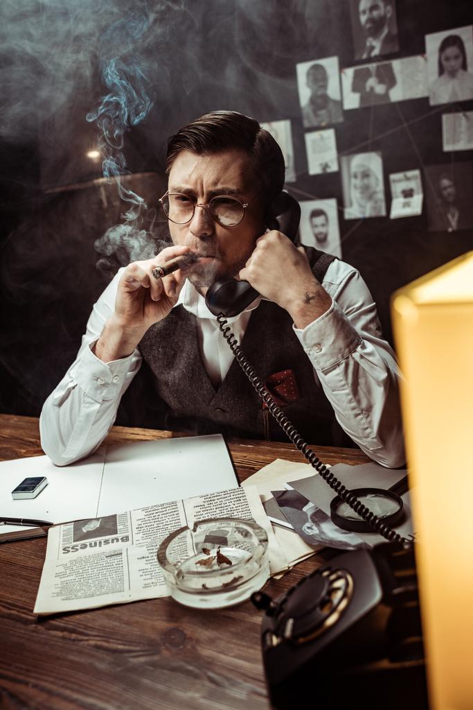 Détective pensif dans des lunettes parlant au téléphone dans un bureau sombre
 - Photo, image