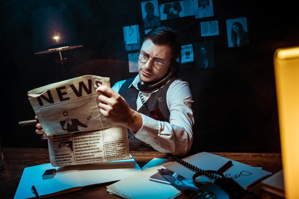 Skoncentrowany detektyw w okularach czytanie gazety i rozmawianie przez telefon - Zdjęcie, obraz