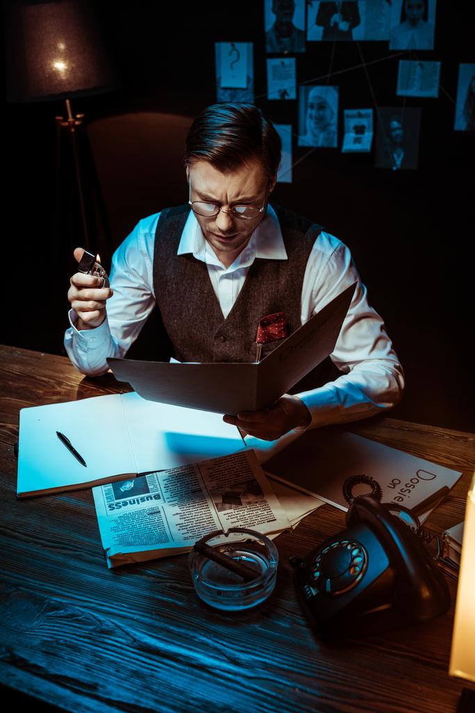Vue en grand angle d'un détective concentré dans des lunettes lisant un dossier dans un bureau sombre
 - Photo, image