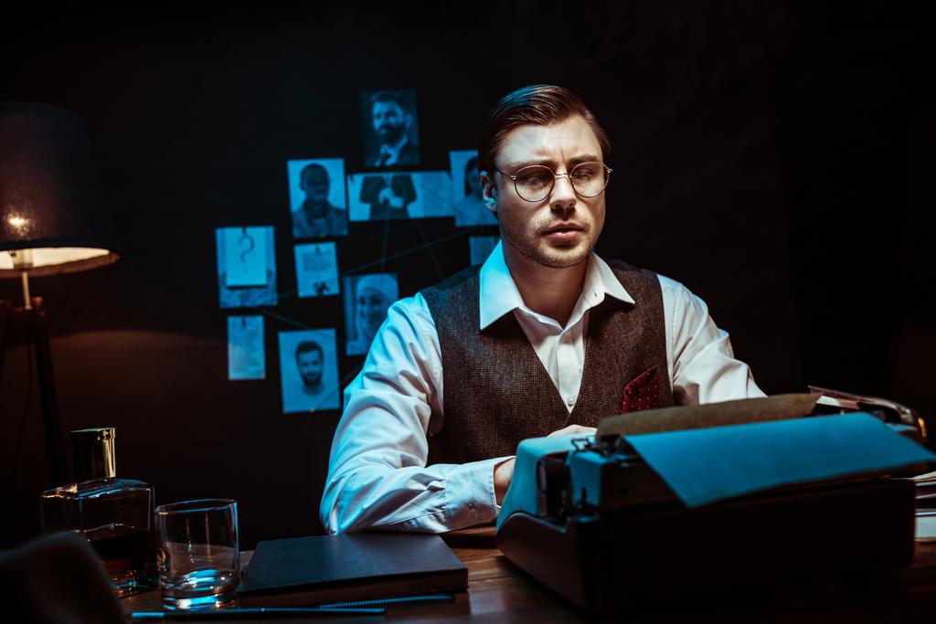 Detective concentrado en gafas usando máquina de escribir en oficina oscura
 - Foto, Imagen