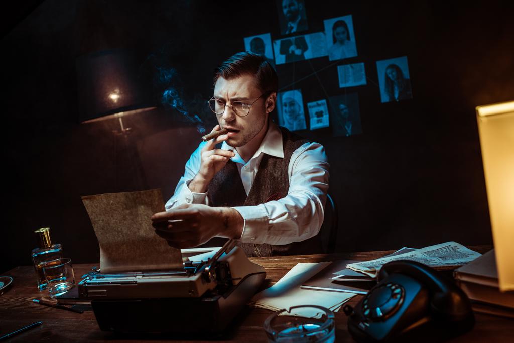 Detective in occhiali fumare sigaro mentre si utilizza la macchina da scrivere in ufficio scuro
 - Foto, immagini