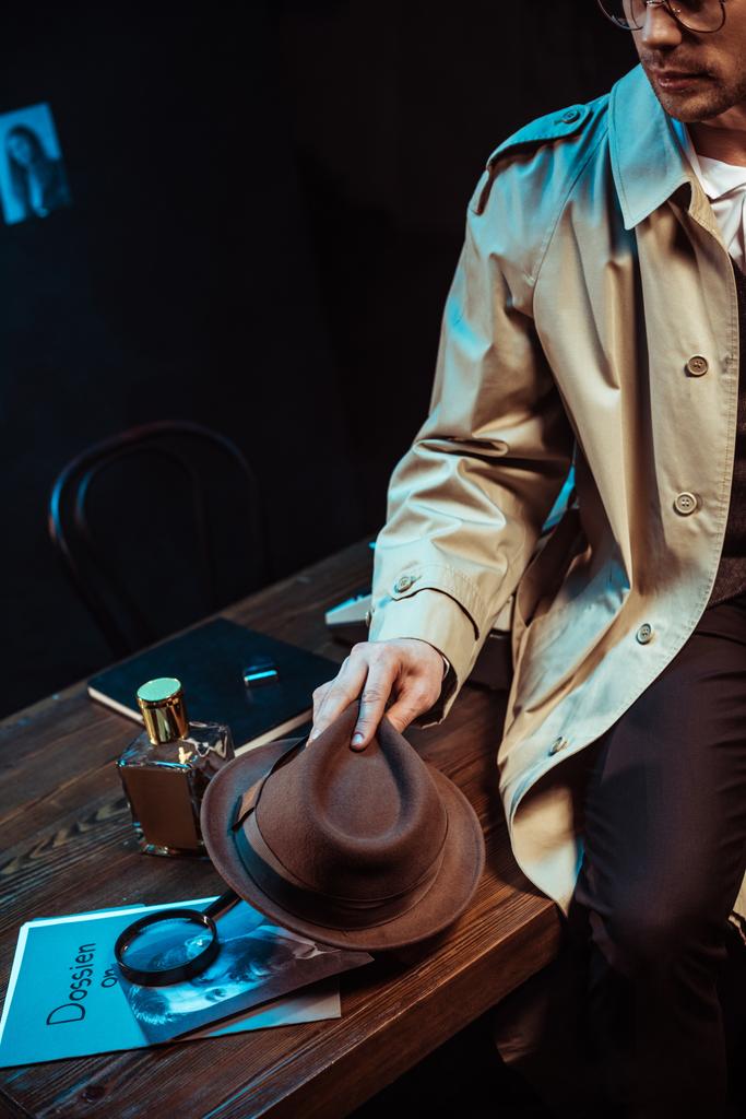 Vista ritagliata del detective in trench seduto sul tavolo e con cappello in mano
 - Foto, immagini
