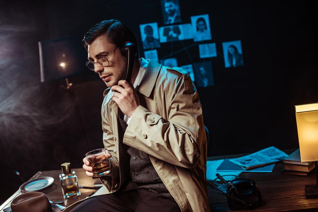 Detektív a szemüveg beszél telefonon és gazdaságban üveg konyak - Fotó, kép