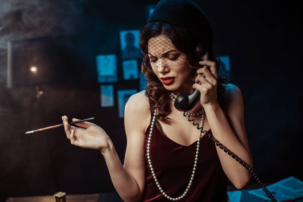 Droevige aantrekkelijke vrouw met mondstuk dat op telefoon in donker Bureau spreekt - Foto, afbeelding