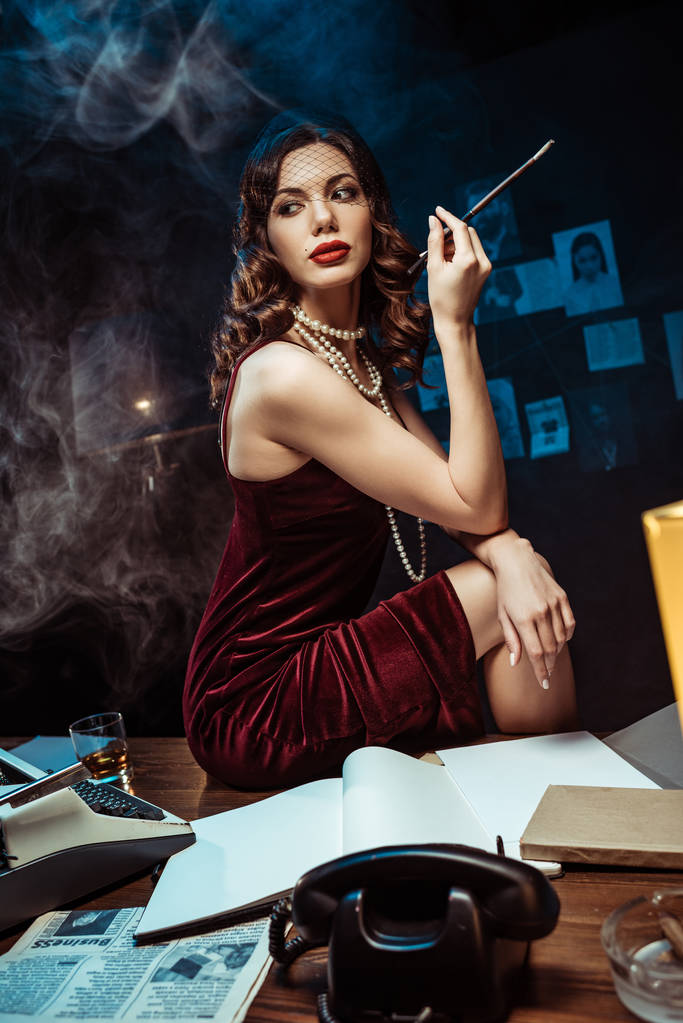 Kaunis nuori nainen mekko tilalla suukappale istuessaan pöydällä pimeässä toimistossa
 - Valokuva, kuva