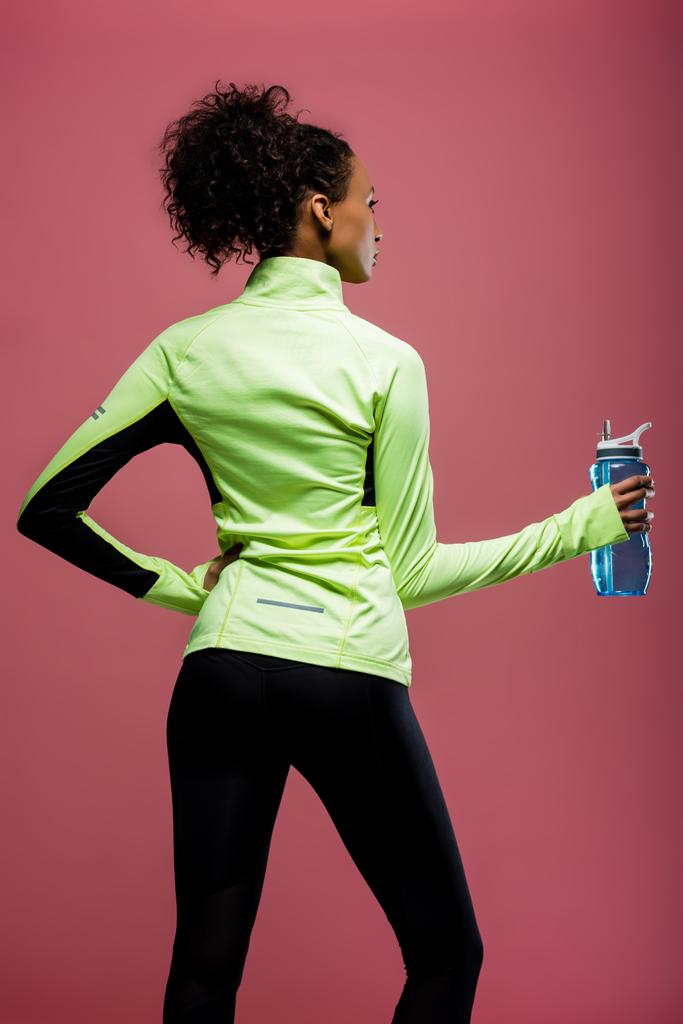 Rückseite der afrikanisch-amerikanischen Sportlerin in Trainingsjacke mit Sportflasche isoliert auf braun - Foto, Bild