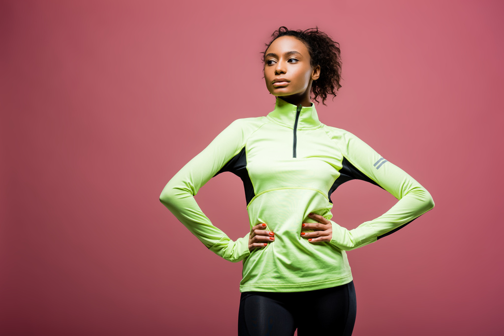 bella sportiva afroamericana in giacca da pista con le mani akimbo posa isolata sul rosa
 - Foto, immagini