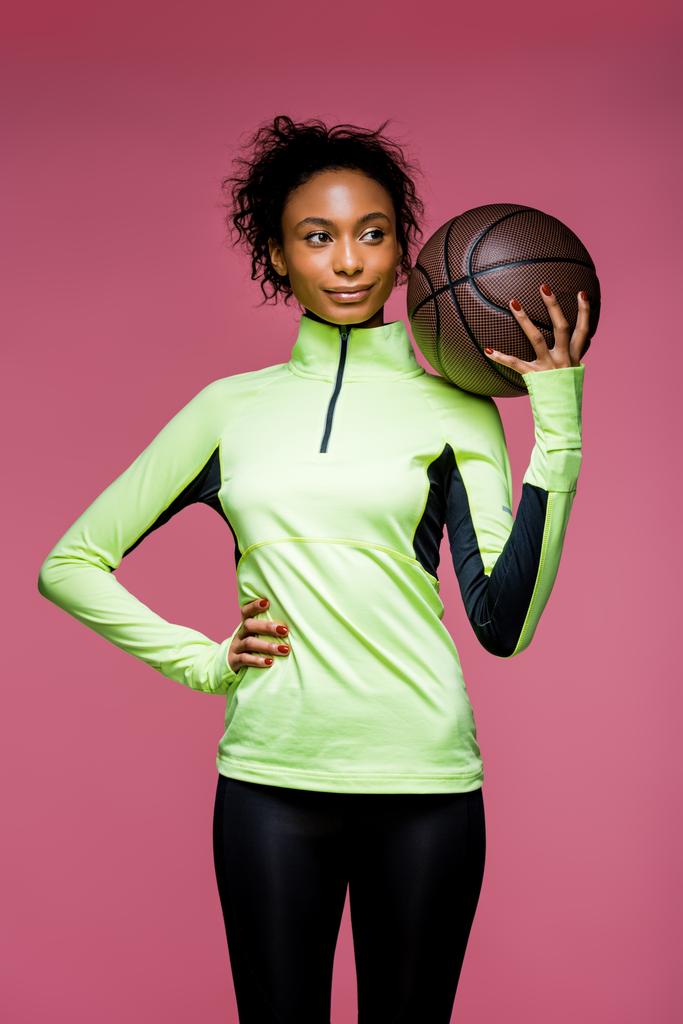 beautiful african american sportswoman with hand on hip holding basketball isolated on pink - Photo, Image