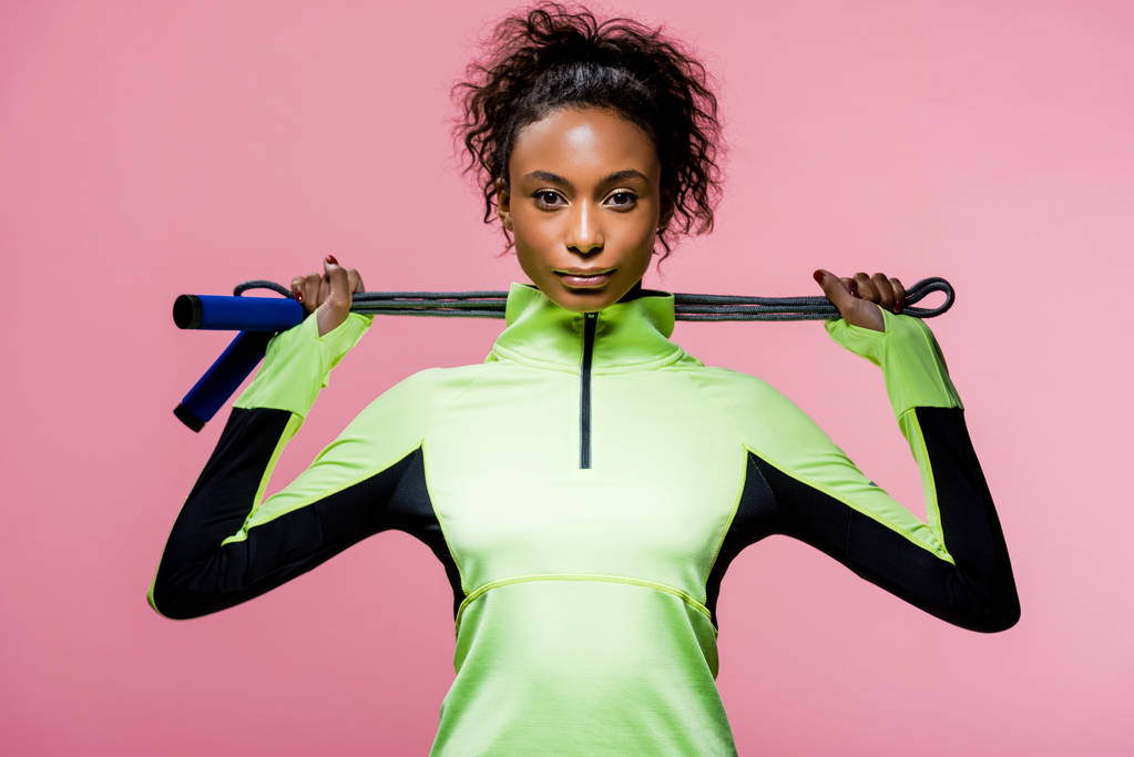 beautiful african american sportswoman looking at camera while posing with skipping rope isolated on pink - Photo, Image