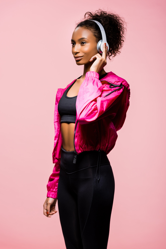 όμορφη αφρικανική αμερικανική αθλήτρια στα ακουστικά Ψάχνετε απομονωμένα μακριά σε ροζ - Φωτογραφία, εικόνα