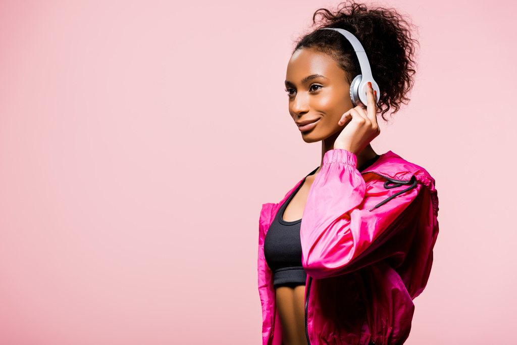 krásné africká americká sportovkyně ve sluchátkách při pohledu od izolovaných na růžový s kopií prostor - Fotografie, Obrázek