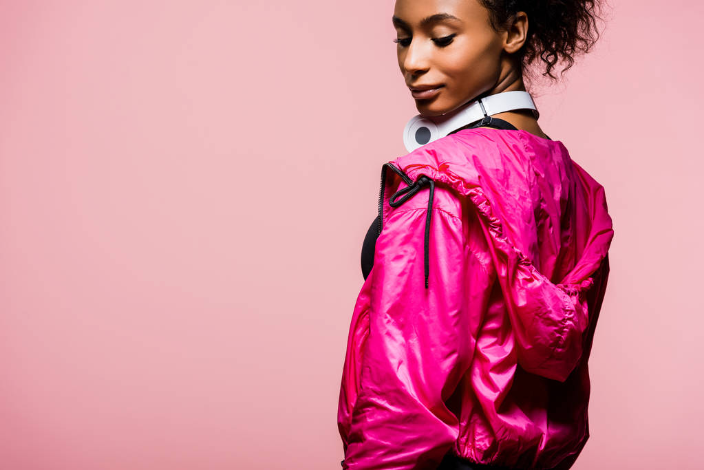 bellissima sportiva afroamericana in giacca a vento con cuffie isolate su rosa con spazio copia
 - Foto, immagini