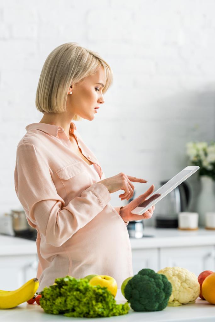 ελκυστική έγκυος γυναίκα χρησιμοποιώντας ψηφιακό δισκίο στην κουζίνα  - Φωτογραφία, εικόνα