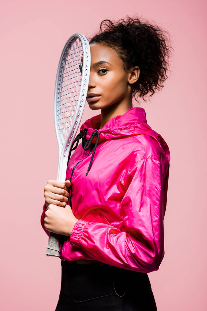 schöne afrikanisch-amerikanische Sportlerin mit Tennisschläger und Blick in die Kamera isoliert auf rosa - Foto, Bild