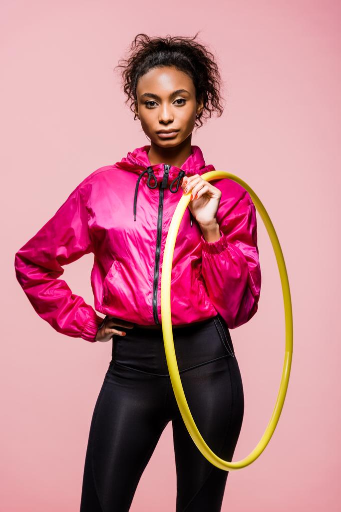 bela esportista afro-americana olhando para a câmera e segurando hula hoop isolado em rosa
 - Foto, Imagem