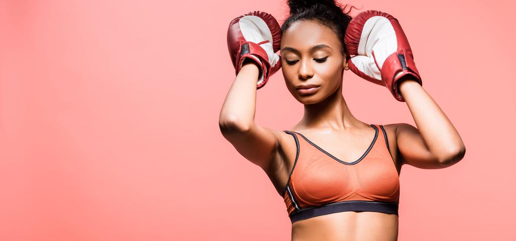 panoramic shot of beautiful african american sportswoman in boxing gloves isolated on coral with copy space - Photo, Image
