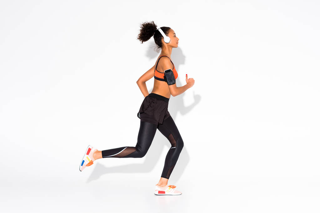 sportos afro-amerikai sportoló, fejhallgató és smartphone karszalag futó fehér - Fotó, kép