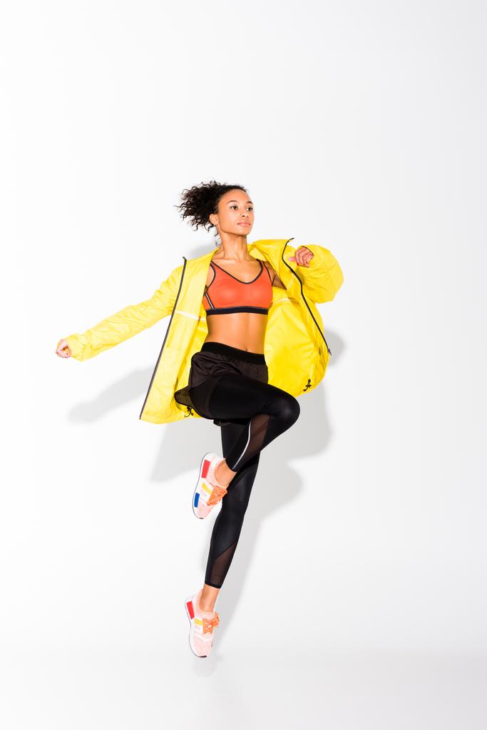 athletic african american sportswoman in yellow sports jacket jumping on white - Photo, Image