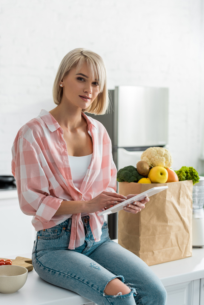 attractive woman using digital tablet near paper bag with ingredients   - Photo, Image