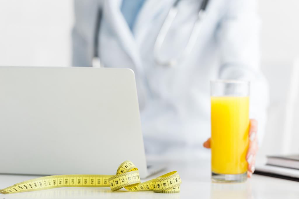 обрезанный вид диетолога, держащего стакан свежего апельсинового сока возле измерительной ленты
  - Фото, изображение
