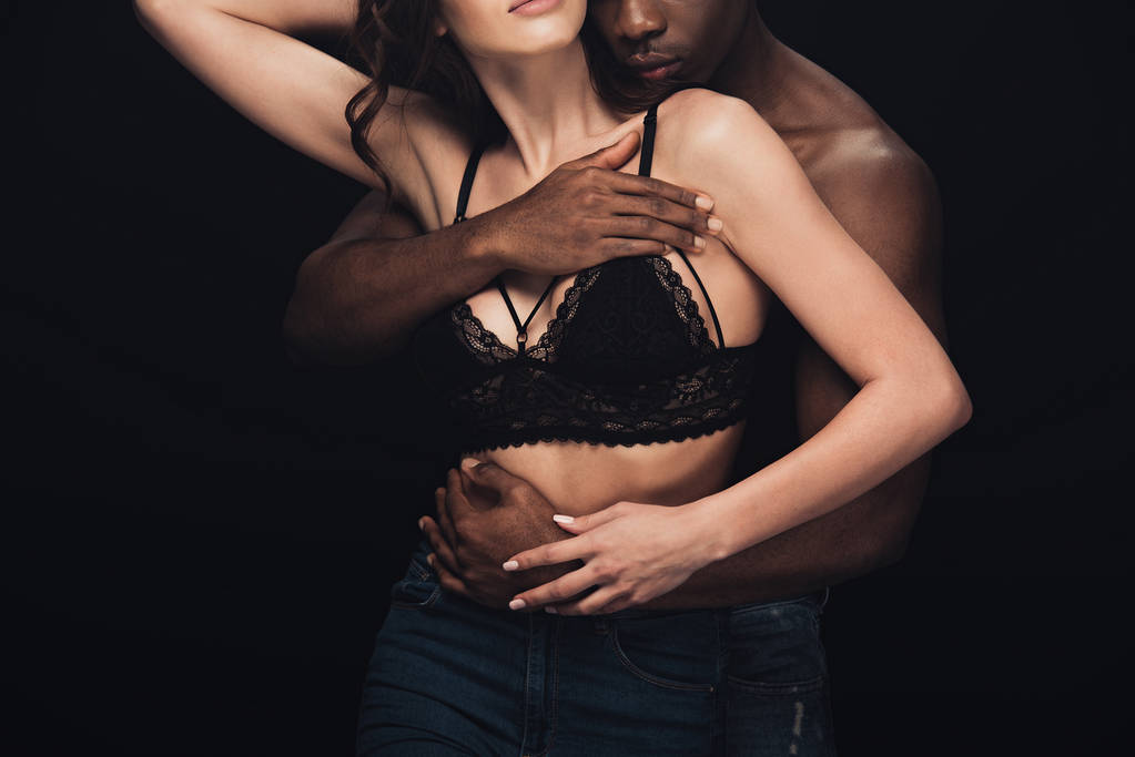 ランジェリーでセクシーな女性を抱きしめたアフリカ系アメリカ人男性のクロップドビューを黒に分離 - 写真・画像