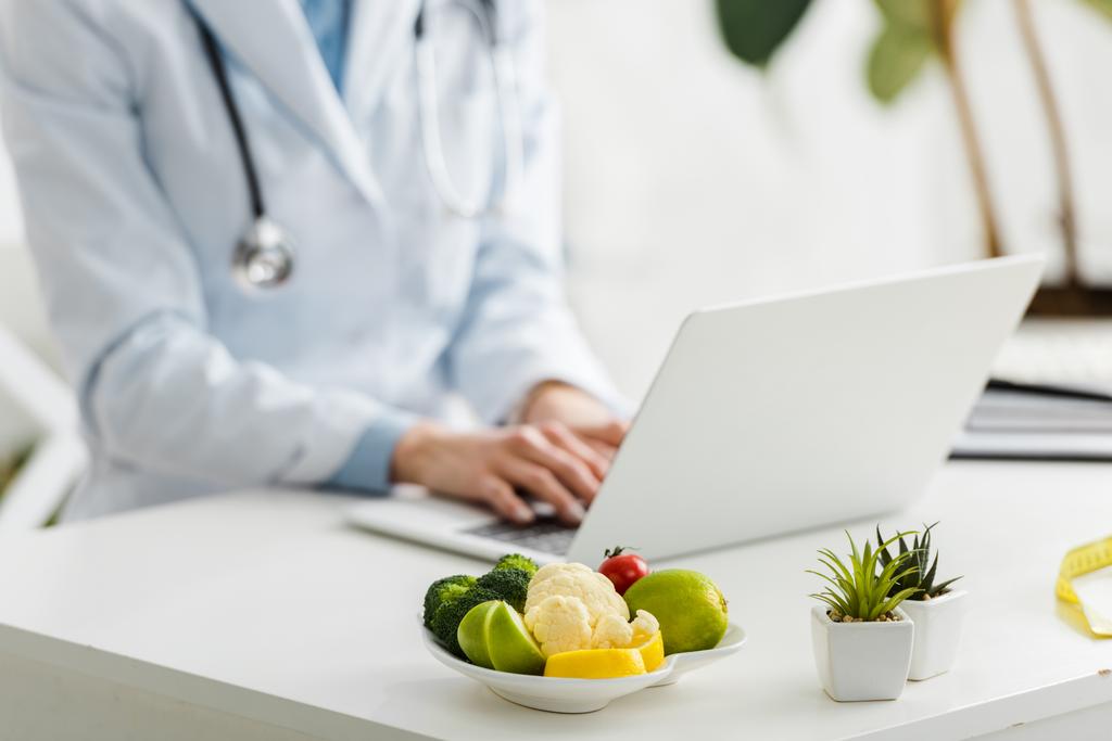 有機食品とプレートの近くにノートパソコンを使用して栄養士のクロップビュー - 写真・画像