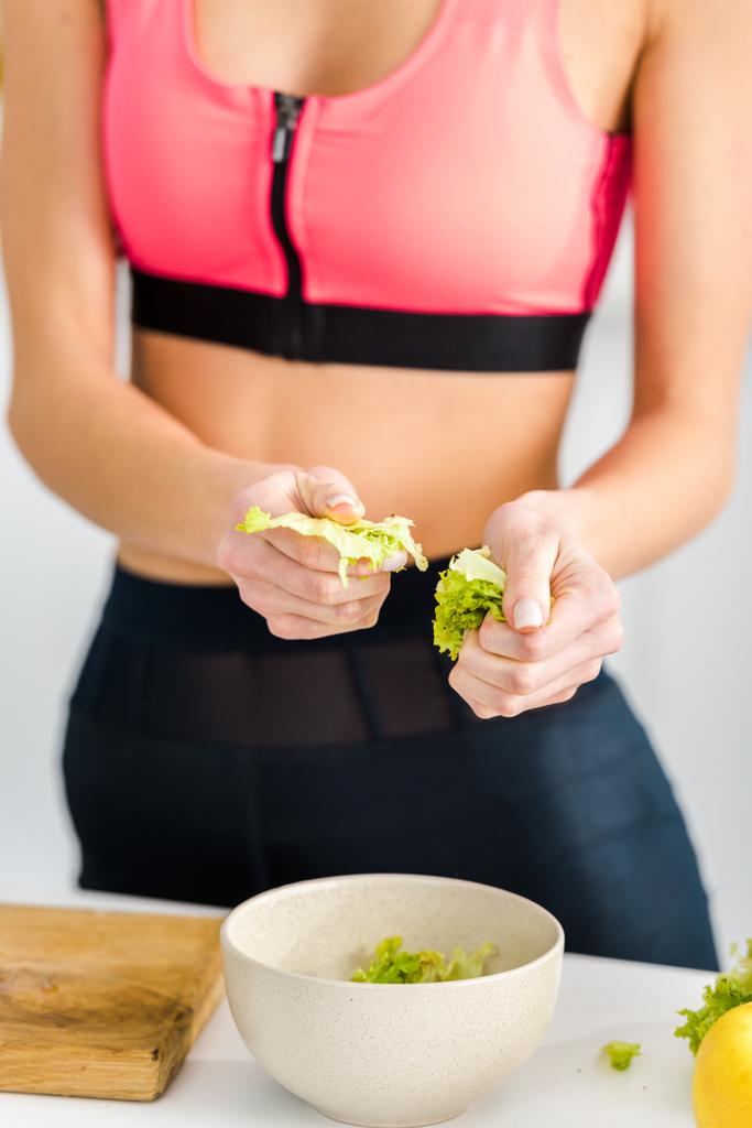 vista cortada de mulher em sportswear segurando folhas de salada perto da tigela
 - Foto, Imagem