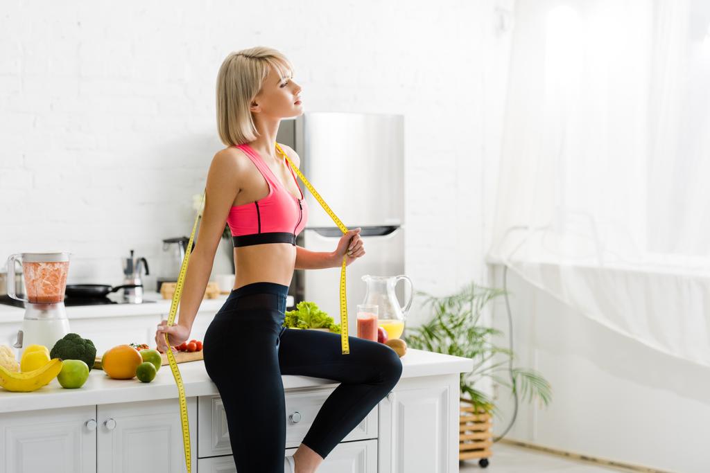 привлекательная блондинка в спортивной одежде держит скотч рядом с ингредиентами на кухне
  - Фото, изображение