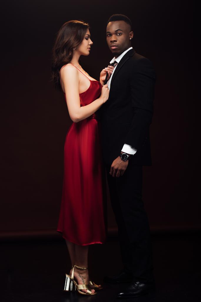 beautiful woman in red dress posing with african american man in suit isolated on black - Photo, Image