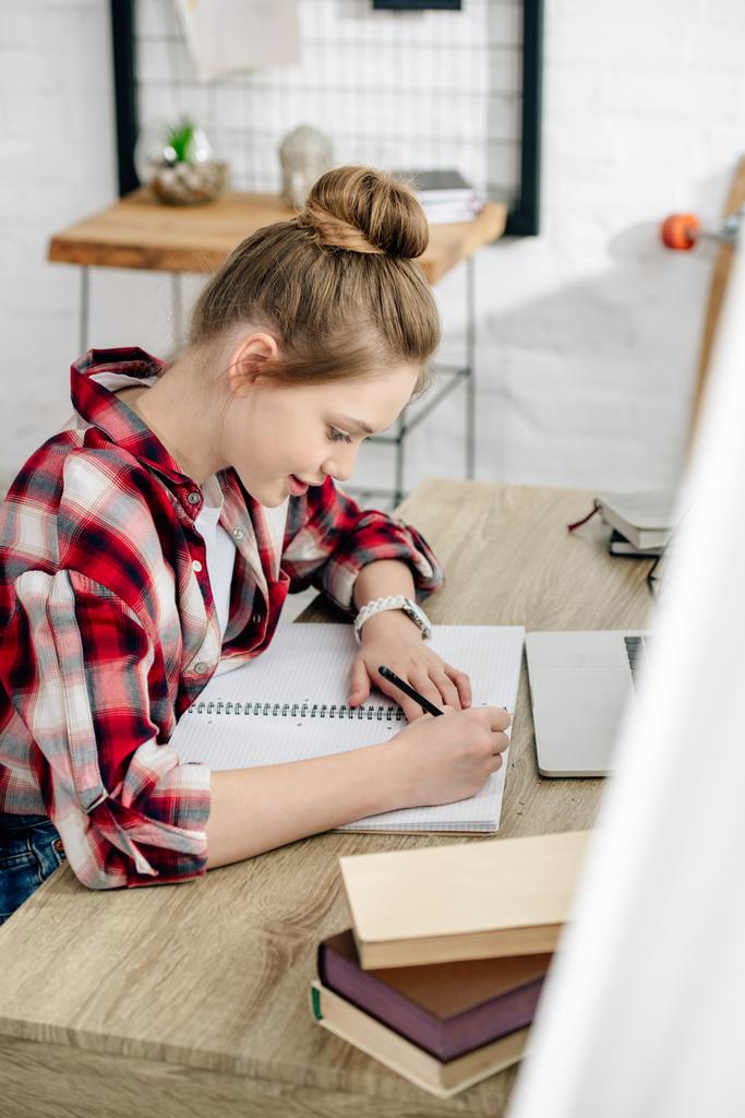 Teenager im karierten Hemd schreibt während der Hausaufgaben in Notizbuch - Foto, Bild