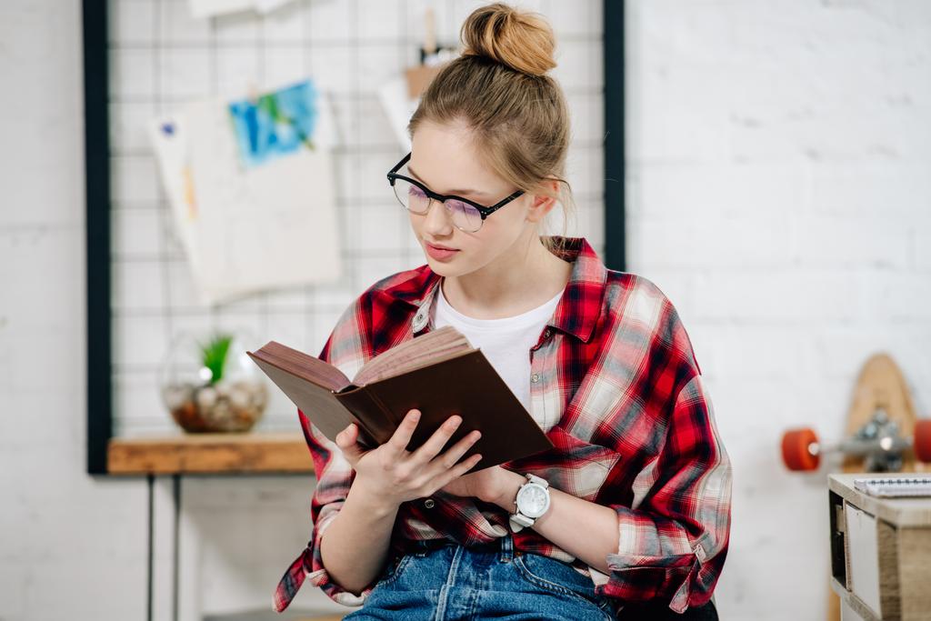 Miúdo adolescente curioso em óculos e livro de leitura de camisa quadriculada
 - Foto, Imagem