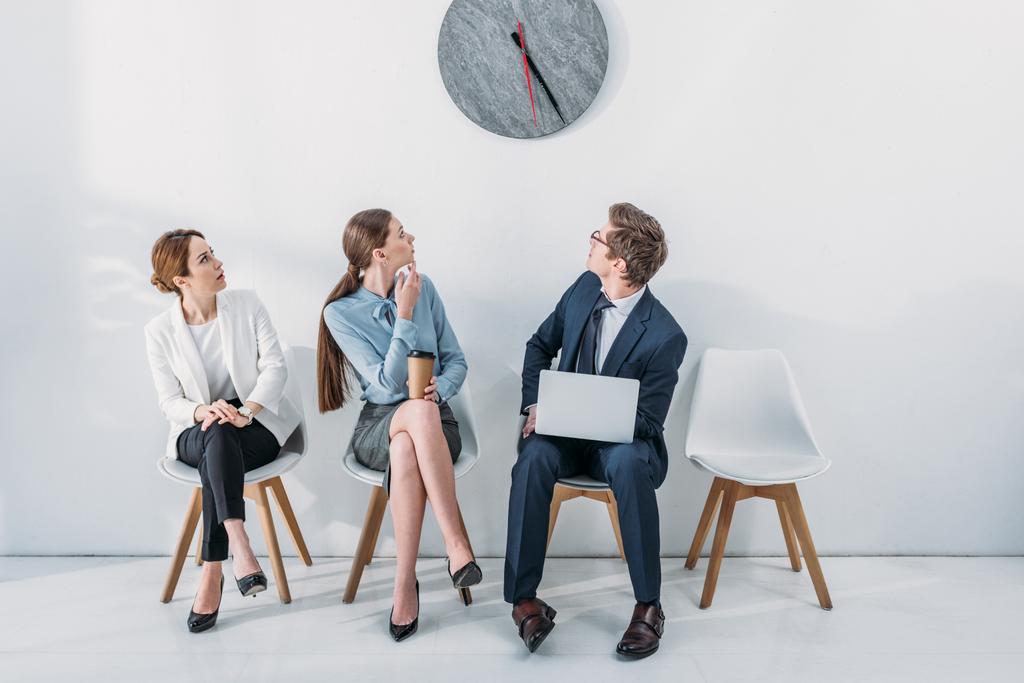 mujeres y hombres con portátil mirando el reloj mientras espera entrevista de trabajo
  - Foto, Imagen