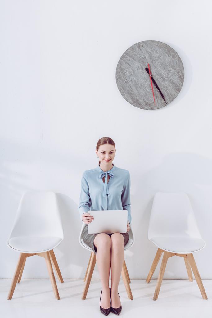 χαρούμενη γυναίκα κάθεται στην καρέκλα με φορητό υπολογιστή ενώ περιμένει συνέντευξη δουλειά  - Φωτογραφία, εικόνα