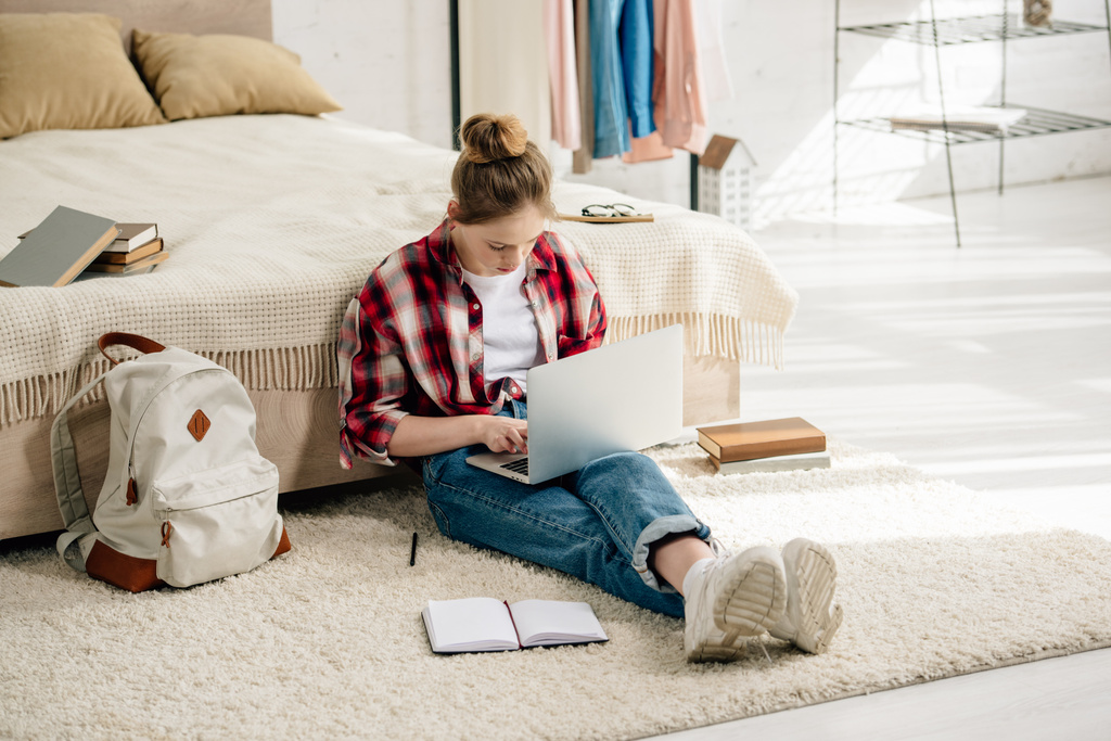 Adolescente con laptop e libri seduto su tappeto e fare i compiti
 - Foto, immagini