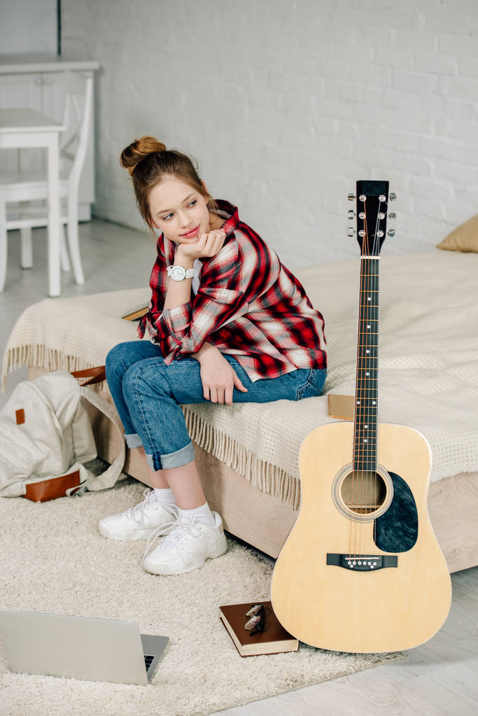 Iloinen teini istuu sängyllä ja katselee akustista kitaraa
 - Valokuva, kuva