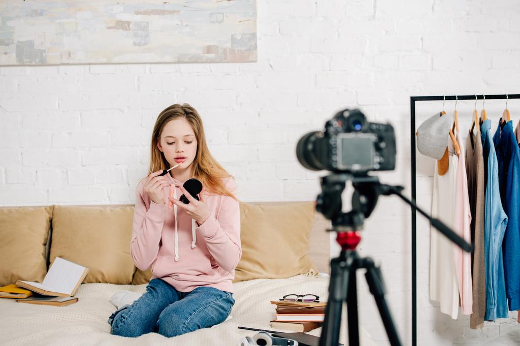 Teen blogger κάθεται στο κρεβάτι και να κάνει μακιγιάζ μπροστά από βιντεοκάμερα - Φωτογραφία, εικόνα