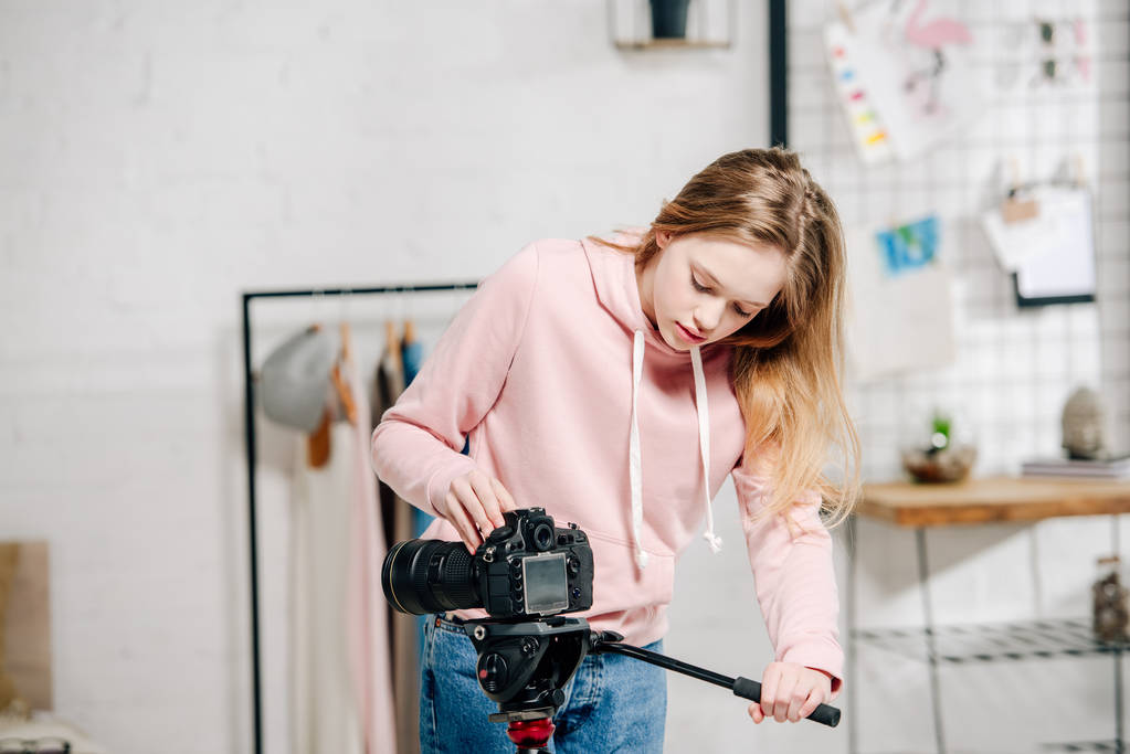 Teenager-Bloggerin im rosafarbenen Kapuzenpulli richtet Videokamera zu Hause ein - Foto, Bild