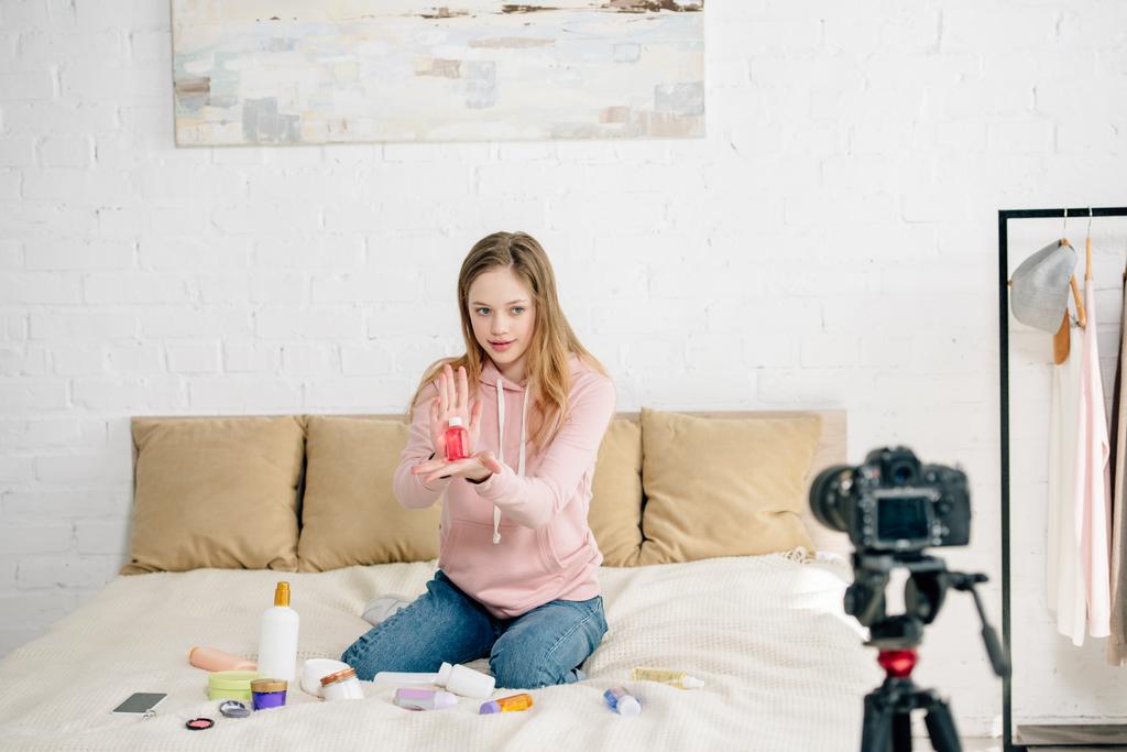 Teenage blogger zittend op bed en beauty producten te tonen aan de camera - Foto, afbeelding