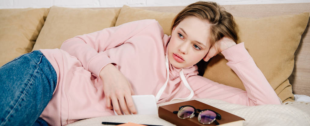 Panoramiczny strzał zmęczony nastolatek z książki i smartphone leżącego na łóżku - Zdjęcie, obraz