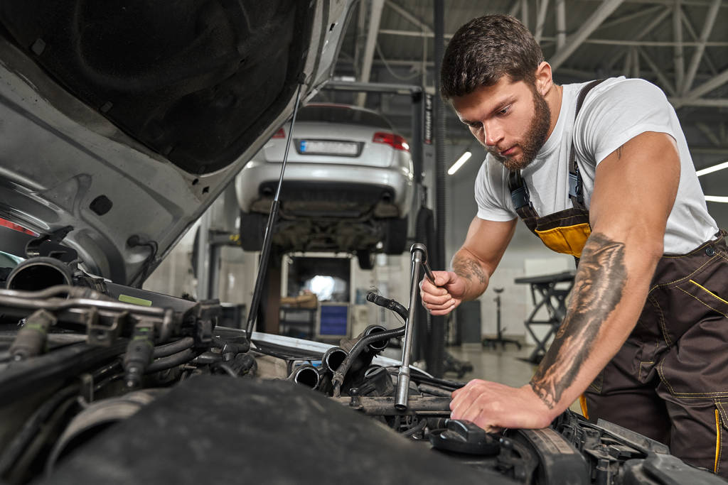 Strong man wearing coveralls repairing engine in automobile - Photo, Image